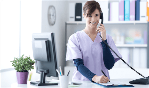 white female nurse smiling and in clinic talking to patient on phone