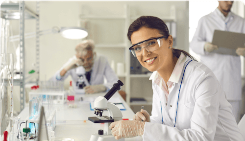 female lab assistant smiling and using microscope in lab