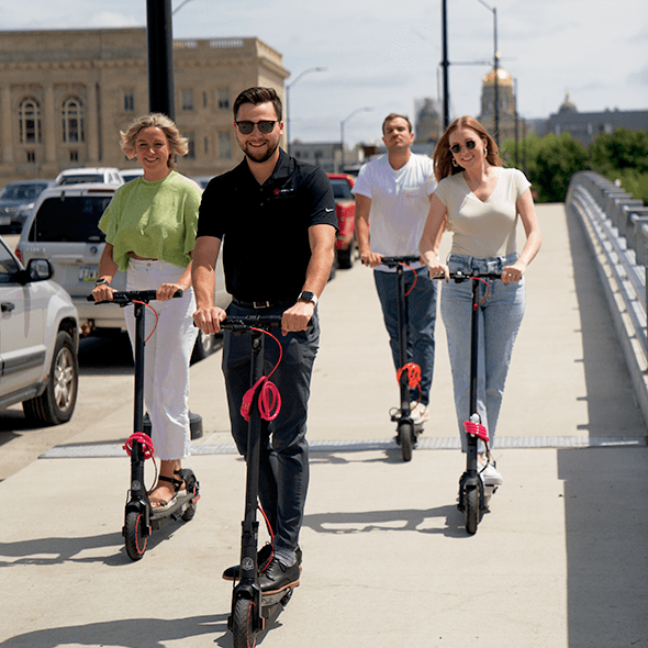 Cole Horton, Sales enablement specialist, Jackie White and Liz Fleming, Business Development Representatives, Jon Choda, HR Assistant, riding electric scooter in downtown Des Moines, IA